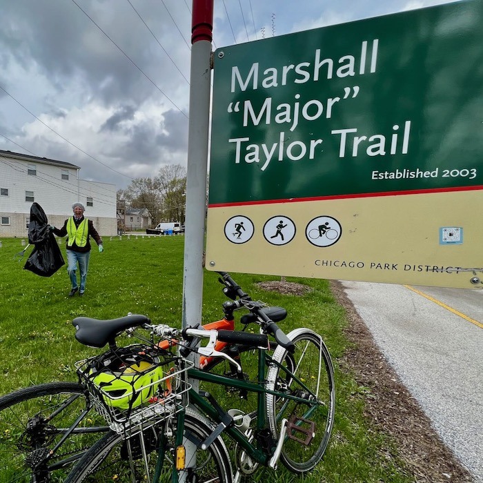 Joanne with trash bag, two bikes and Major Taylor Trail sign